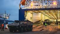 In der Morgendämmerung steht eine Fähre mit geöffneter Rampe in einem Hafen und Fahrzeuge fahren aus dem Schiffskörper