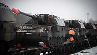 Auf einem Bahnwaggon stehen hintereinander aufgereiht Panzerhaubitzen