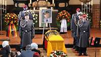Acht Soldaten stehen in einer Kirche neben einem Sarg, der mit der Bundesdienstflagge umhüllt ist.