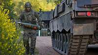Ein Soldat läuft an einem gepanzerten Fahrzeug vorbei und trägt ein Sprenggeschoss