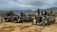 Deutsche und griechische Soldaten begutachten drei Schützenpanzer Marder im Gelände.