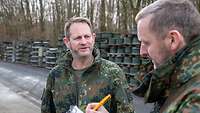 Ein Soldat steht vor gelagerten Felgen und unterhält sich mit einem anderen Soldaten, der ein Klemmbrett in der Hand hält.