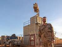 Soldat vor dem Kamerasystem Ein Soldat steht vor sandfarbenen Containern, die übereinandergestapelt sind. Darauf befindet sich das Kamerasystem.