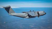 Ein A400M ist in der Luft. Von beiden Flügeln aus gehen Betankungsschläuche nach hinten.