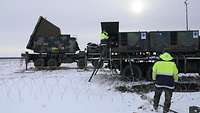 Ein Soldat steht vor einem großen Stromerzeugungsaggregat, das auf einem verschneiten Feld steht. 
