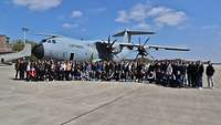 Zahlreiche Mädchen und Jungen stehen auf einem Flugfeld vor einem A400M-Transportflugzeug mit geöffneter Tür
