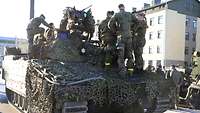 Soldatinnen und Soldaten stehen auf einem Panzer und schauen sich das Fahrzeug an. 