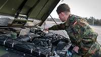 Ein Soldat steht vor einer geöffneten Motorhaube und checkt verschiedene Flüssigkeiten am Motor.