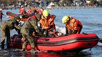 Zwei Soldaten und zwei Angehörige des Rettungsdienstes sichern eine Verletzte auf einem Boot.