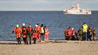 Personen verschiedener Rettungsorganisationen versorgen Schiffbrüchige am Strand
