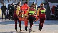 Vier Personen in Ausrüstung für die Wasserrettung transportieren einen Verletzten auf einer Liege