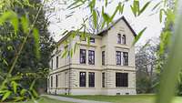Das Bild zeigt eine beigefarbene Villa – die Villa Plaut auf dem Gelände der Führungsakademie der Bundeswehr