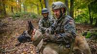 Ein Soldat hockt neben seinem Diensthund und öffnet das Geschirr des Hundes.
