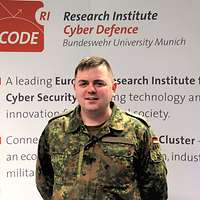 Soldat vor einem Logo des Forschungsinstitut CODE der Bundeswehr-Universität München.