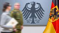 Symbolbild Spitzenstellen Ein Soldat und eine Zivilistin (mit einer Urkunde in der Hand) vor einer Wand mit dem Bundesadler