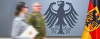 Symbolbild Spitzenstellen Ein Soldat und eine Zivilistin (mit einer Urkunde in der Hand) vor einer Wand mit dem Bundesadler