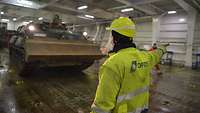 Ein Schiffsmitarbeiter in Warnjacke weist einen Panzer per Handzeichen im Schiff seinen Platz zu.