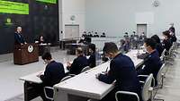 Ein Militär trägt vor einer Gruppe weiterer Militärs in einem Saal vor