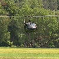 Mehrzweckhubschrauber Bell UH-1 D in der Luft vor einen grünen Wald.
