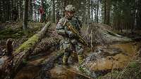 Ein bewaffneter Soldat überquert einen Bach im Wald
