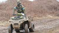Ein Soldat steht auf einem Quad. Vorne hat er seine Waffe und seinen Rucksack festgeschnallt.