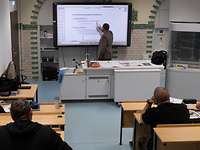 Ein Mann steht an einem Smartboard und zeigt auf etwas während vier Männer zuhören.