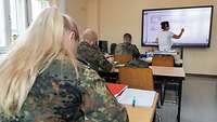 Soldatinnen und Soldaten sitzen in einem Unterrichtsraum mit Blick zum Smartboard.