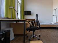 Ein Zimmer mit Bett, Schreibtisch, Drehstuhl und einem Fernseher.