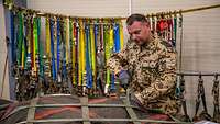 Alles sitzt fest Ein Soldat prüft die Verzurrgurte an einer Palette, im Hintergrund hängen mehrere Verzurrgurte.