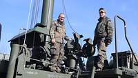 Zwei Soldaten stehen auf einem militärischen Gerät.