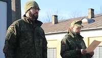 Hauptmann Christina H. steht neben einem Soldaten und liest eine Urkunde vor. 