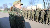 Hauptmann Christina H. steht vor einer Gruppe angetretener Soldatinnen und Soldaten.