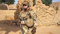 Der Soldat steht in einem malischen Dorf.