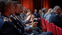 Soldaten sitzen auf roten Stühlen und applaudieren.