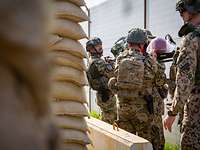Die Soldaten suchen mit der Trage für den Verwundeten hinter Sandsäcken und einem Bunker Schutz.