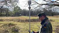 Im Vordergrund eine Drohne, im Hintergrund Soldaten die mit Vermessungsgerät arbeiten.