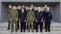Soldaten stehen nebeneinander und blicken in die Kamera. Im Hintergrund befindet sich ein Gebäude.