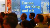 Im Vordergund das Plenum zur Eröffnungsrede, im Hitergrund iein Banner mit dem Namn der Ausstellung "Euroa, der Krieg und ich"