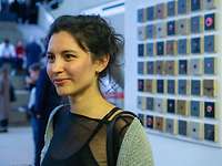 Eine Frau vor einem Kunstwerk aus viereckigen Bodenstücken und verschiedenfarbigen Knöpfen 