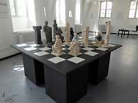 Ein überdimensionales Schachbrett mit schwarzen und weißen Figuren in einem Raum.
