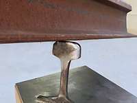 Ein Stahlträger balanciert auf einem kleinen Fußstück aus Metall. 