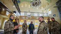 Vier Soldaten und zwei Männer sprechen miteinander in einer Moschee.