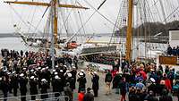 Auslandsausbildungsreise der ,,Gorch Fock'' Viele Menschen und musizierende Soldaten auf einer Hafenpier neben einem dreimastigen Segelschiff