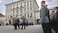 Vor einer Formation auf einem Schlosshof schreiten zwei Soldaten und ein Zivilist die Front ab.