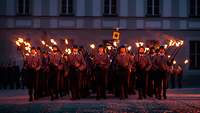 Eine Formation Soldaten steht nachts auf einem Schlosshof mit Fackeln.