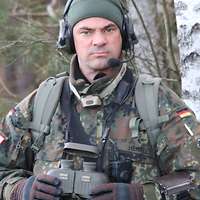 Ein Soldat mit grüner Mütze und Sprechsatz schaut stirnrunzelnd in die Kamera.