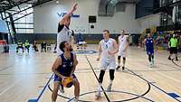 Ein Spieler mit Ball in der Hand täuscht einen Sprung, der Verteidiger springt bereits in die Luft. 