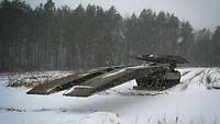 Das Brückenlegesystem Leguan verlegt seine Panzer-Schnellbrücke in einer verschneiten Landschaft.