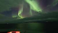 Über dem Wasser erscheinen bei Nacht Polarlichter am Sternenhimmel.