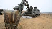 Ein Pionierpanzer Kodiak mit ausgefahrener Schaufel und Räumschild steht im Sand.